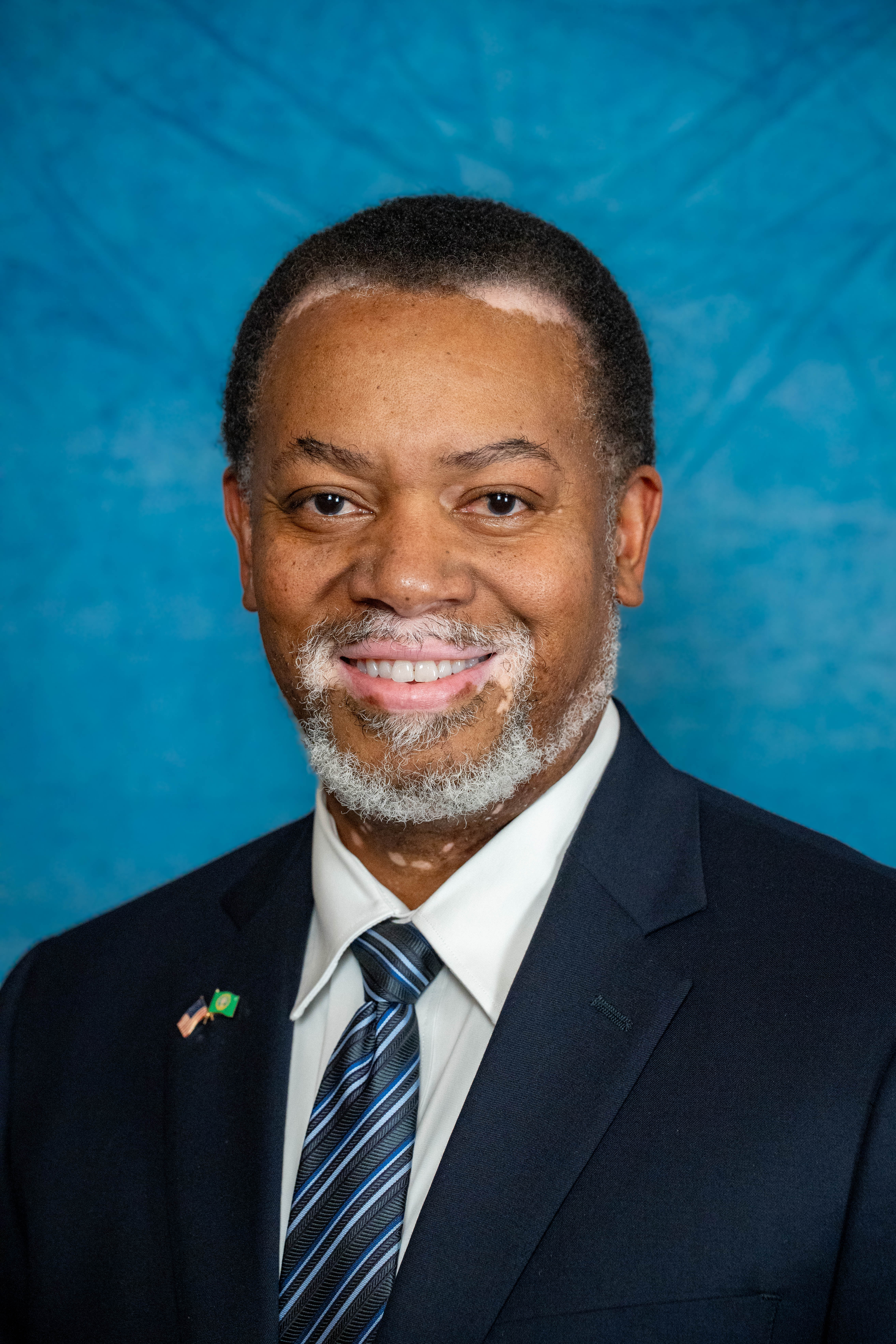 City council headshot — navy suit, flag pin